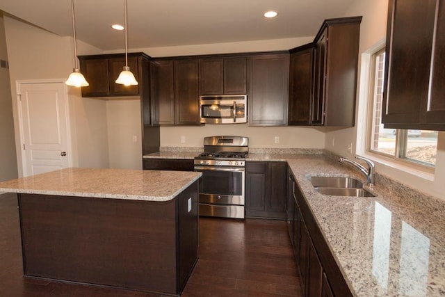 kitchen featuring decorative light fixtures, sink, a center island, light stone counters, and stainless steel appliances