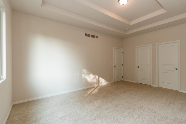 empty room featuring carpet, a raised ceiling, visible vents, and baseboards