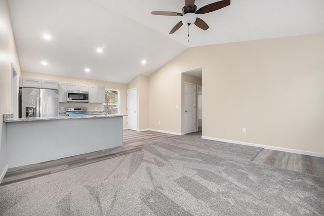 unfurnished living room with ceiling fan, vaulted ceiling, and light carpet