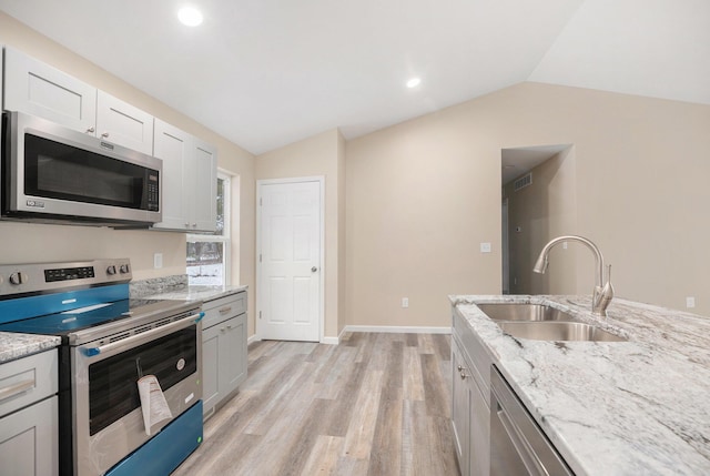 kitchen featuring sink, appliances with stainless steel finishes, light stone counters, white cabinets, and vaulted ceiling