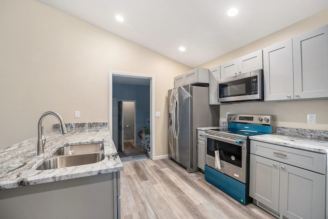 kitchen with sink, vaulted ceiling, light wood-type flooring, appliances with stainless steel finishes, and light stone countertops