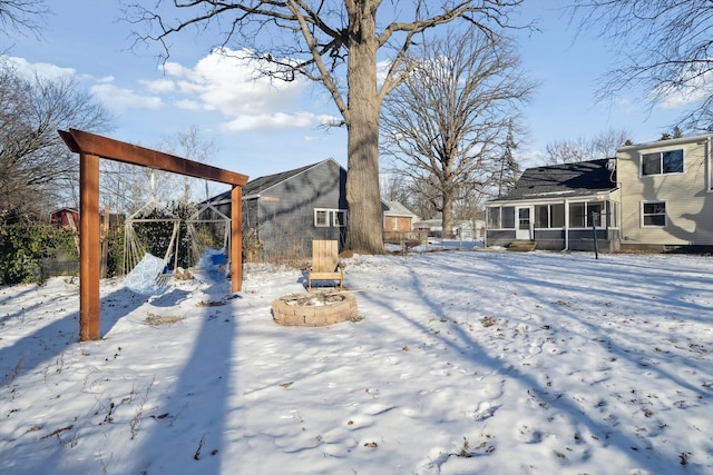 snowy yard with a sunroom and an outdoor fire pit