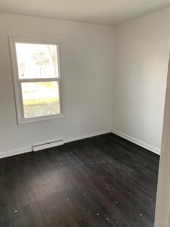 empty room featuring a baseboard heating unit and dark wood-type flooring