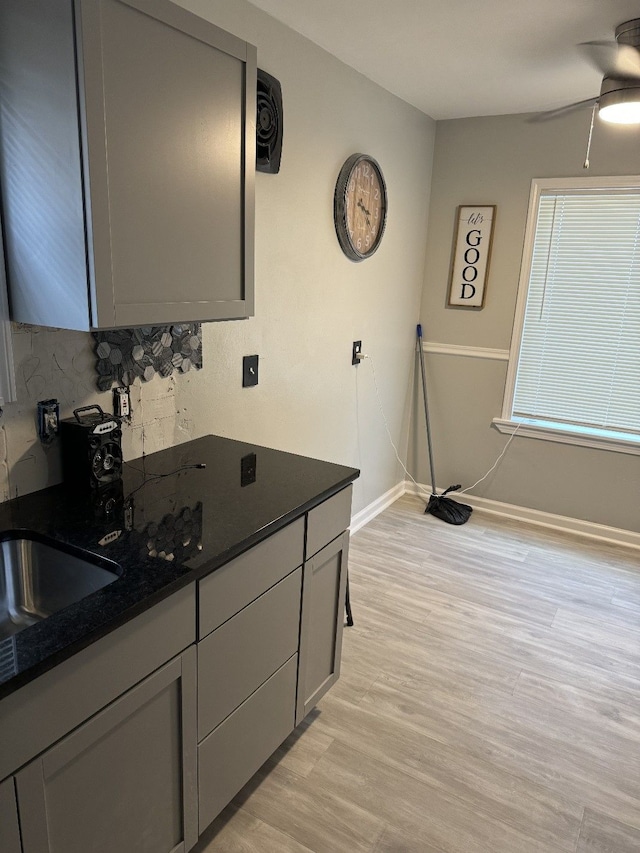 kitchen with ceiling fan, gray cabinets, light hardwood / wood-style flooring, and dark stone countertops