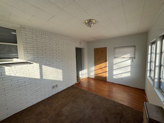 unfurnished room with hardwood / wood-style flooring and brick wall