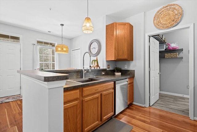 kitchen featuring pendant lighting, sink, stainless steel dishwasher, light hardwood / wood-style floors, and kitchen peninsula