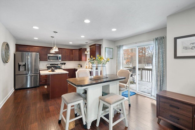 kitchen featuring dark wood-type flooring, appliances with stainless steel finishes, a center island, a kitchen bar, and decorative light fixtures