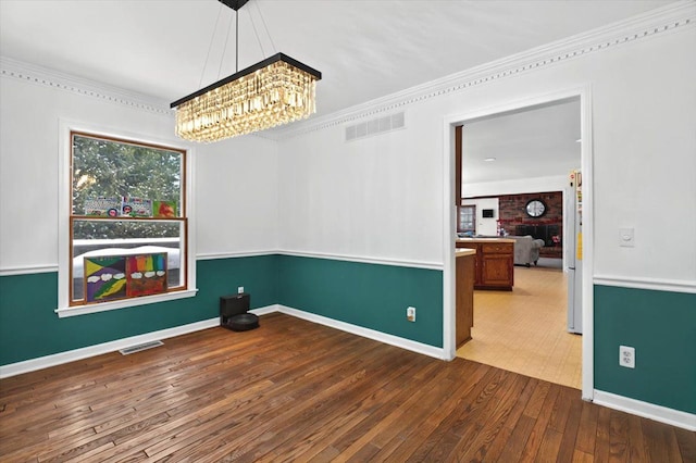 unfurnished dining area featuring baseboards, a notable chandelier, visible vents, and hardwood / wood-style flooring
