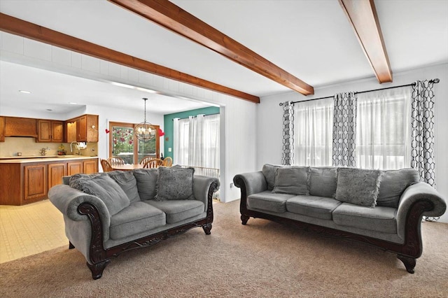 carpeted living room with beam ceiling, sink, and an inviting chandelier