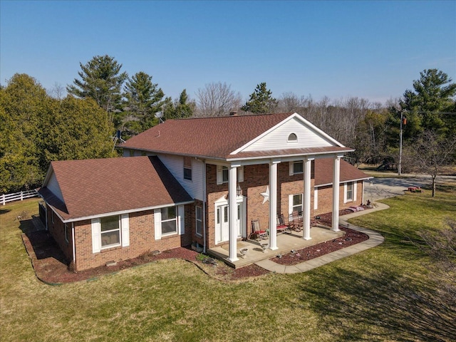 rear view of property with a shingled roof, a lawn, fence, and brick siding