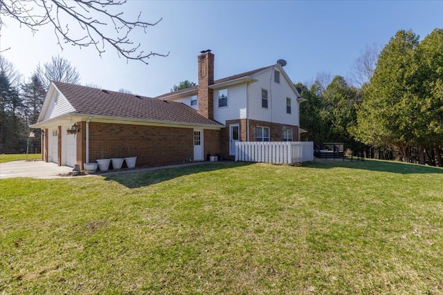 rear view of property with a chimney, driveway, an attached garage, brick siding, and a lawn