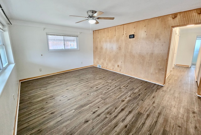 unfurnished room featuring wood-type flooring, wooden walls, and ceiling fan