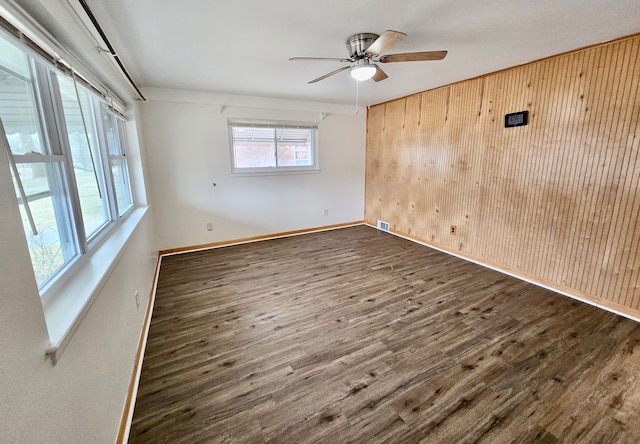 empty room featuring ceiling fan, dark hardwood / wood-style flooring, and wood walls