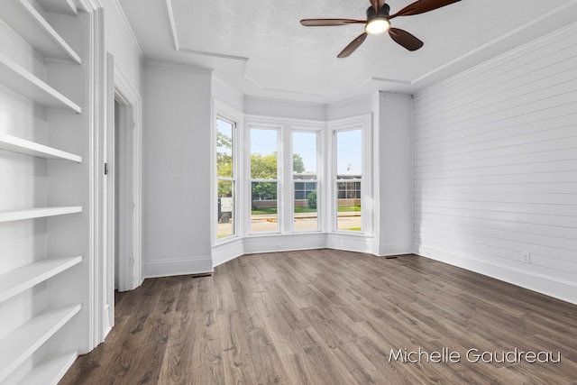 empty room featuring wood-type flooring, ornamental molding, ceiling fan, a textured ceiling, and built in shelves