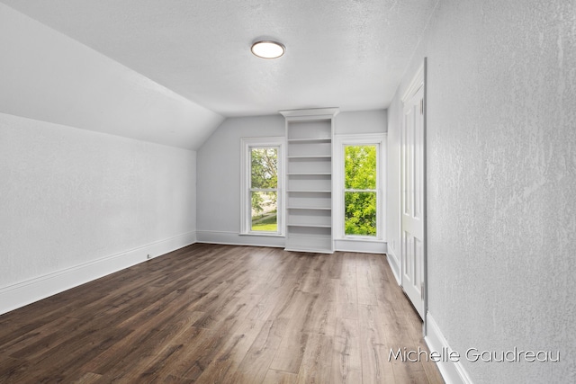 additional living space with lofted ceiling, dark wood-type flooring, and a textured ceiling