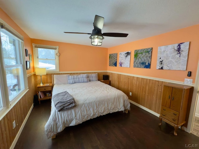 bedroom with dark wood-type flooring, ceiling fan, and wood walls