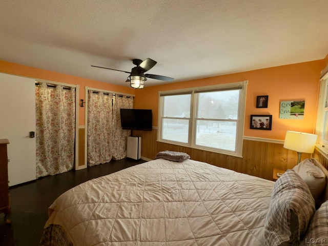 bedroom featuring dark hardwood / wood-style flooring, a textured ceiling, wooden walls, and ceiling fan