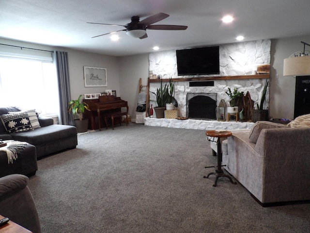 living room featuring a stone fireplace, ceiling fan, and carpet