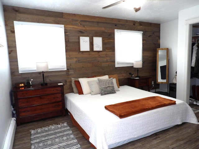 bedroom with multiple windows, baseboard heating, and wood walls