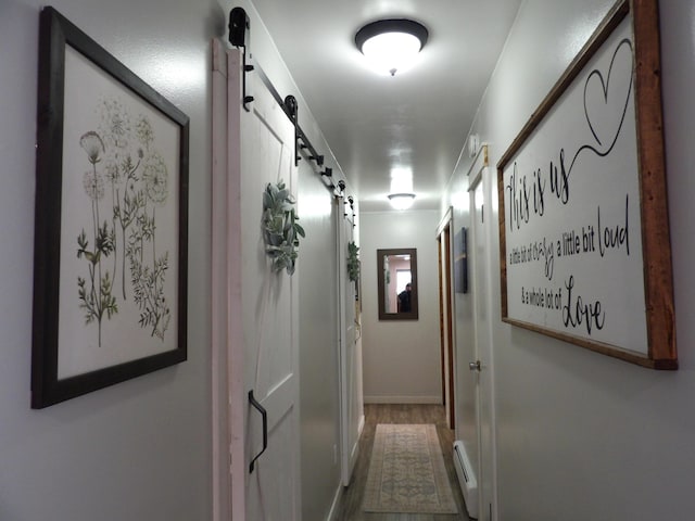 hall with a barn door, hardwood / wood-style floors, and a baseboard heating unit