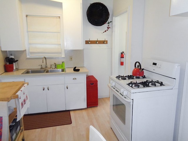 kitchen with white gas range, light hardwood / wood-style floors, sink, and white cabinets