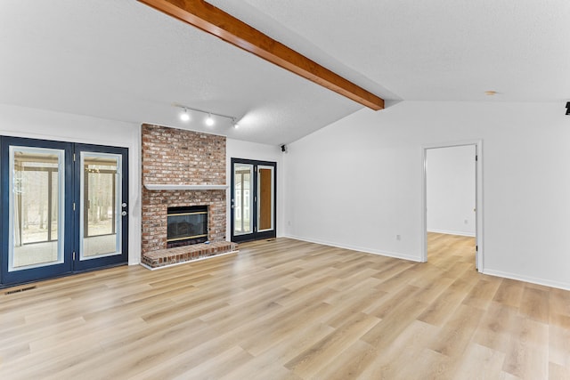 unfurnished living room with a fireplace, lofted ceiling with beams, light hardwood / wood-style floors, a textured ceiling, and french doors