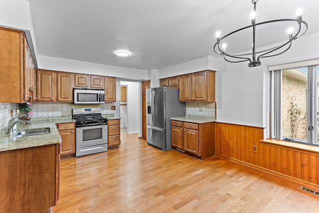 kitchen featuring sink, appliances with stainless steel finishes, hanging light fixtures, light stone counters, and light hardwood / wood-style floors