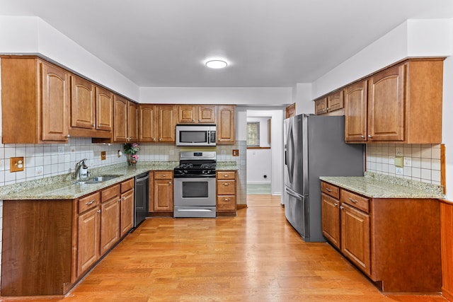 kitchen with sink, light stone counters, light hardwood / wood-style flooring, appliances with stainless steel finishes, and decorative backsplash