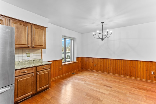 unfurnished dining area with wood walls, a chandelier, and light wood-type flooring