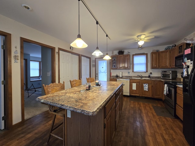 kitchen with a breakfast bar, hanging light fixtures, dark hardwood / wood-style floors, black appliances, and a kitchen island