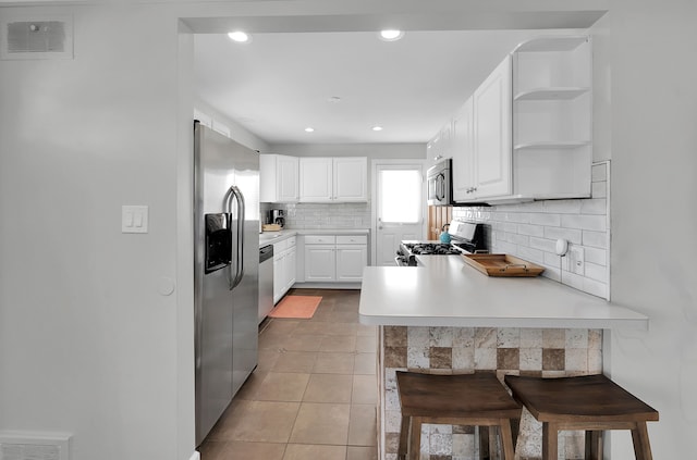 kitchen with light tile patterned flooring, appliances with stainless steel finishes, a breakfast bar area, white cabinets, and decorative backsplash