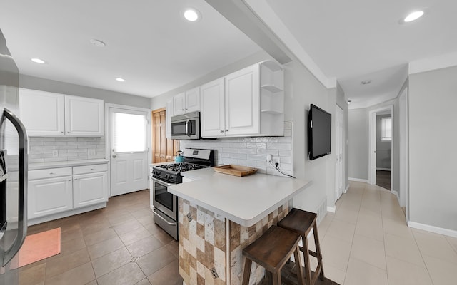 kitchen with a breakfast bar, appliances with stainless steel finishes, white cabinetry, light tile patterned flooring, and decorative backsplash