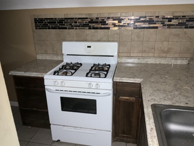 kitchen featuring sink, dark brown cabinets, light tile patterned floors, white range with gas cooktop, and decorative backsplash