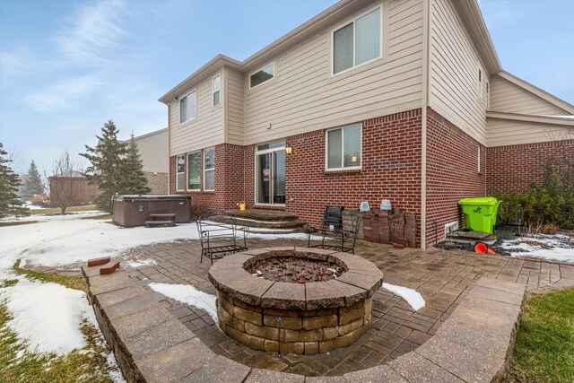 snow covered property with a hot tub, a patio area, and a fire pit