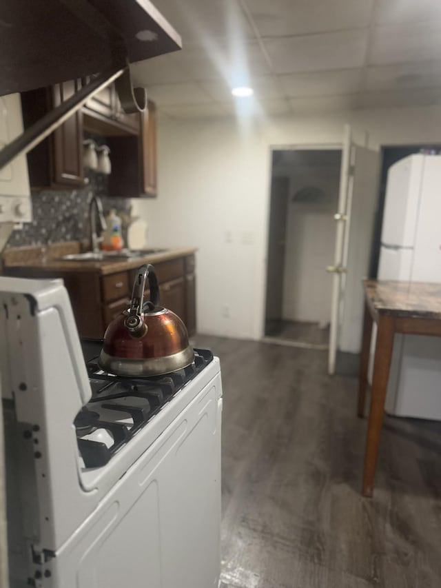 kitchen with a paneled ceiling, tasteful backsplash, sink, gas range gas stove, and dark wood-type flooring