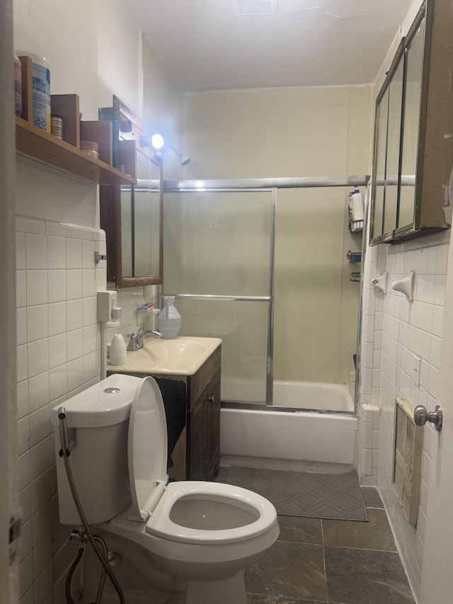 full bathroom with bath / shower combo with glass door, vanity, toilet, and tile walls