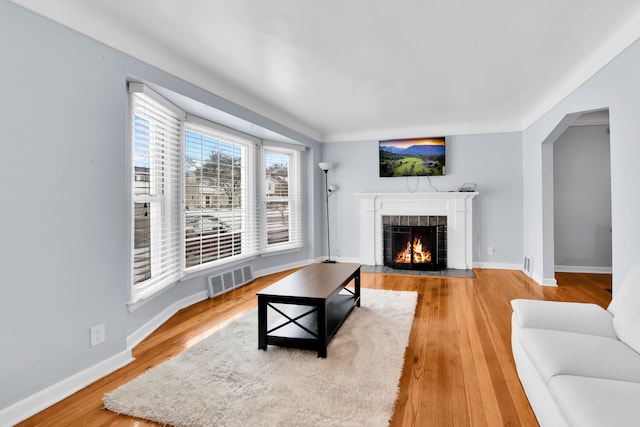 living area featuring baseboards, visible vents, a tiled fireplace, and wood finished floors