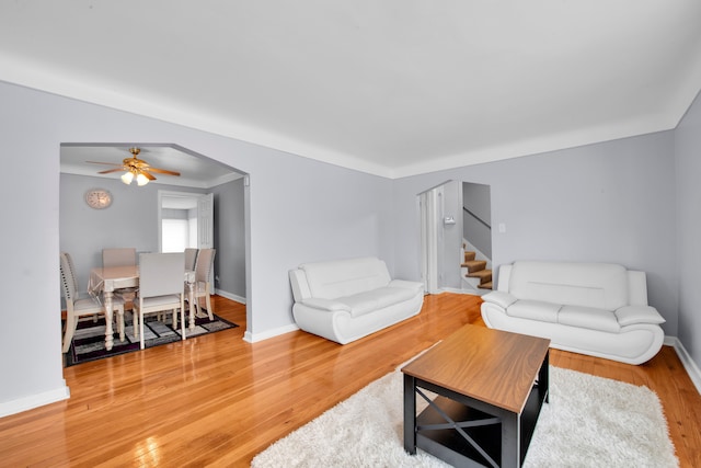 living room featuring arched walkways, wood finished floors, stairs, and baseboards