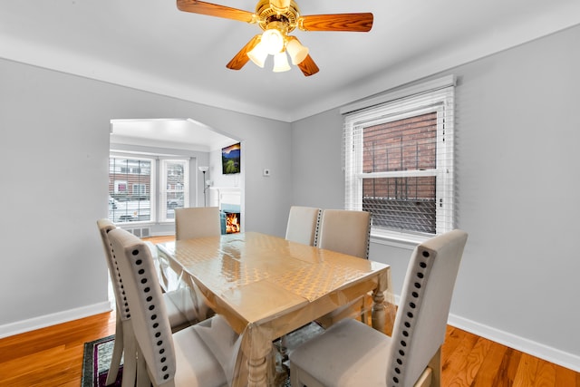 dining space featuring a warm lit fireplace, light wood finished floors, arched walkways, and baseboards