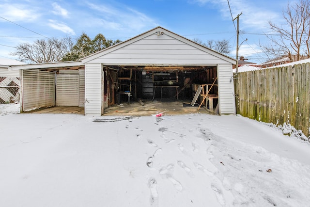 snow covered garage with a garage and fence