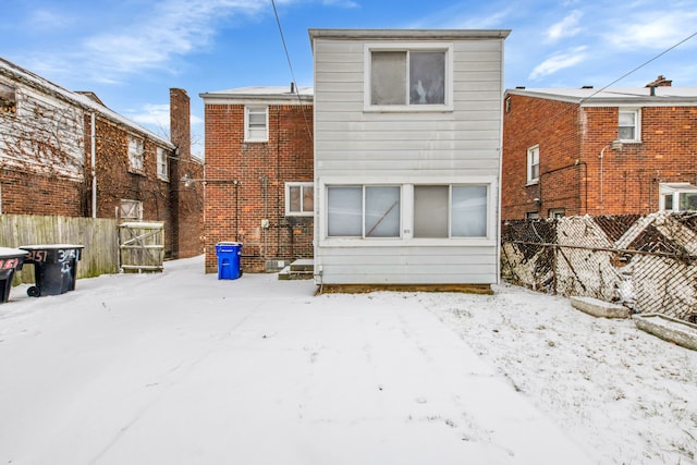 snow covered back of property featuring fence and brick siding