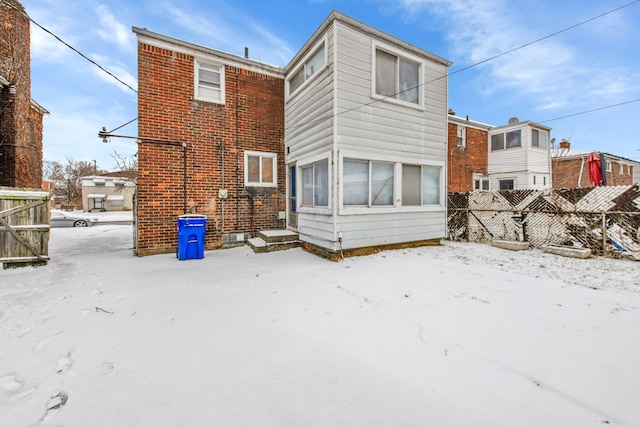 snow covered rear of property with brick siding and fence