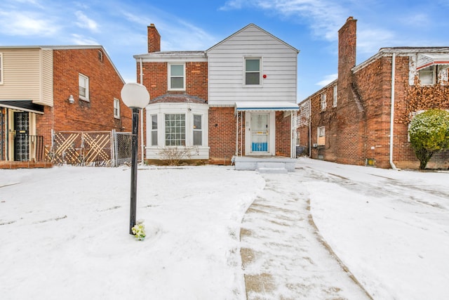 snow covered house featuring brick siding, a chimney, and fence