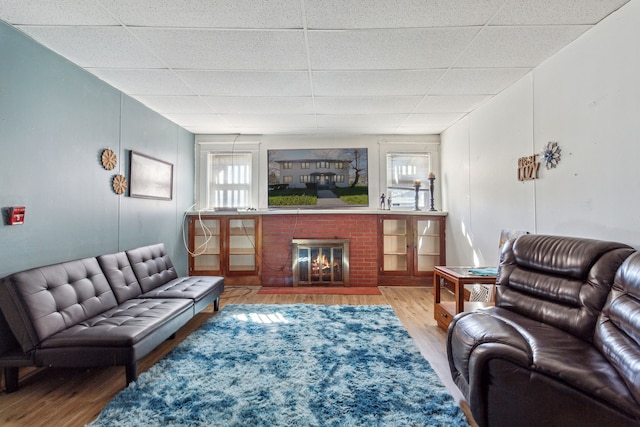 living room featuring a drop ceiling, a brick fireplace, and wood-type flooring