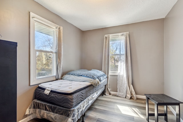 bedroom with a textured ceiling, multiple windows, and light wood-type flooring