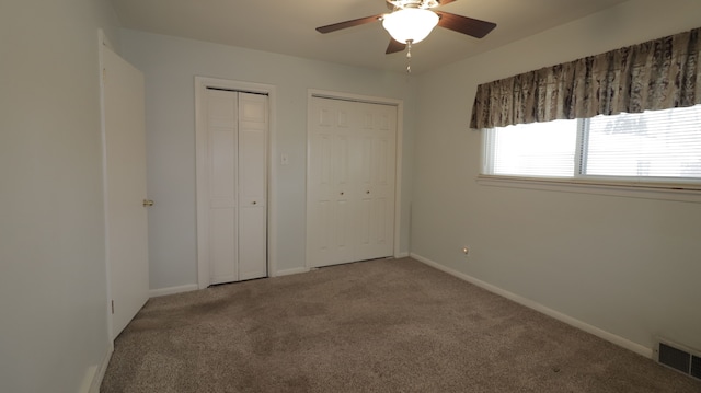 unfurnished bedroom featuring ceiling fan, multiple closets, and carpet flooring