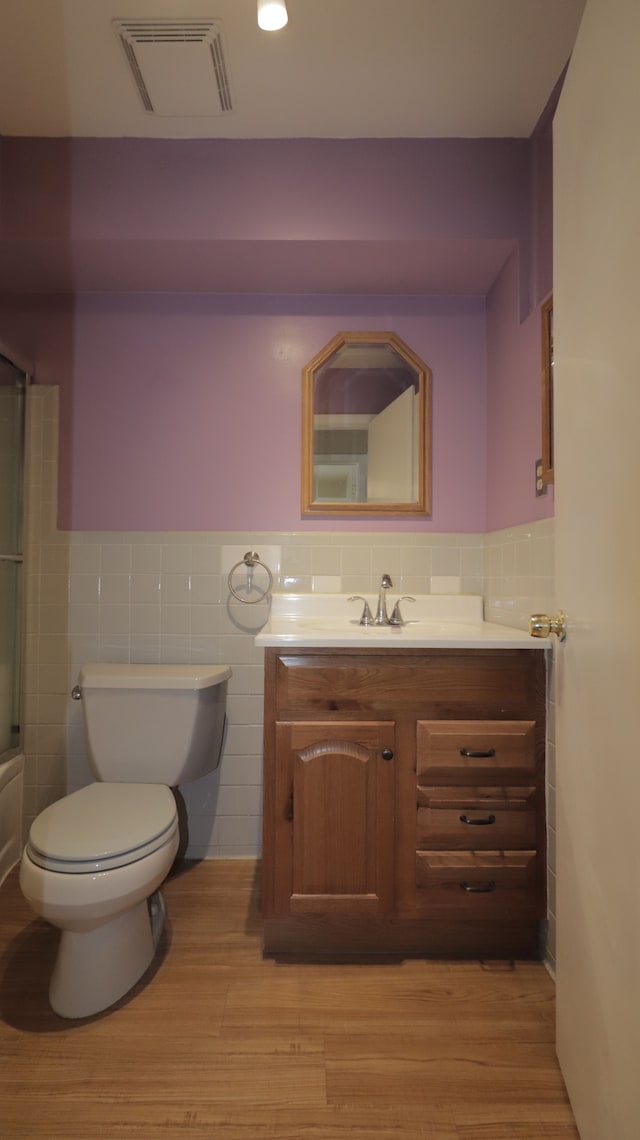 full bathroom featuring wood-type flooring, tile walls, vanity, and toilet