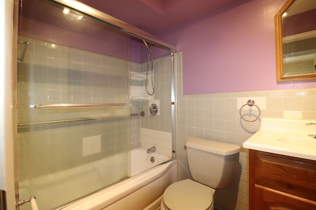 full bathroom featuring vanity, toilet, combined bath / shower with glass door, and tile walls