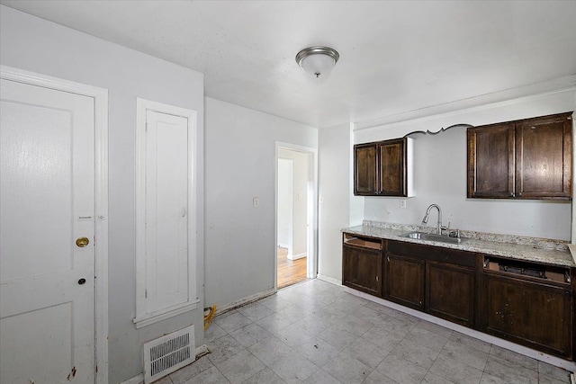 kitchen featuring light stone countertops, sink, and dark brown cabinetry