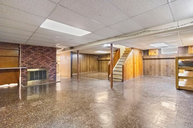 basement with a brick fireplace, a paneled ceiling, and wooden walls